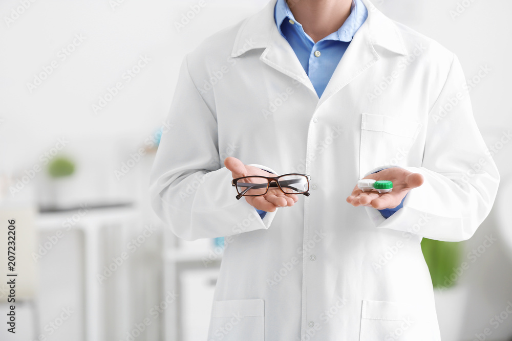 Male doctor holding contact lens case and glasses, indoors Male doctor holding contact lens case and glasses, indoors