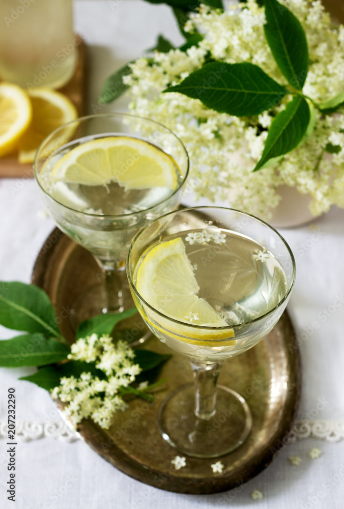 A cool drink with lemon and elderflower syrup in glasses on a metal tray. Rustic style.