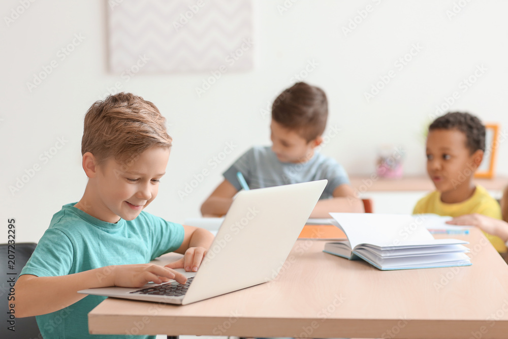 Cute boy with laptop doing homework in classroom at school Cute boy with laptop doing homework in classroom at school