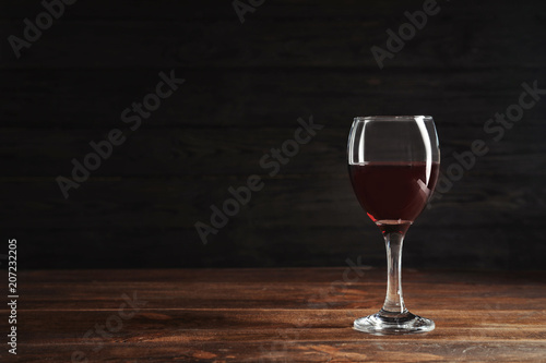 Glass with delicious red wine on table against dark background