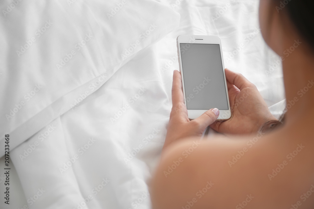 Young woman holding mobile phone with blank screen in hands on bed Young woman holding mobile phone with blank screen in hands on bed