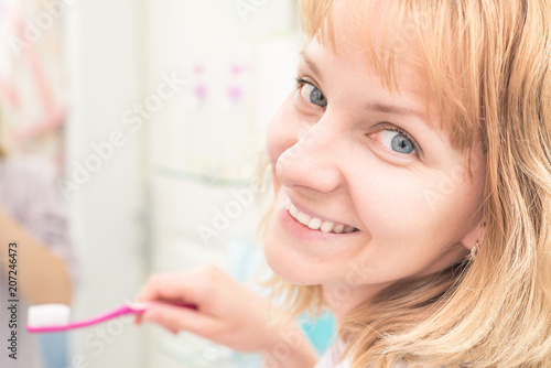Pretty young female looking at camera while brushing teeth in bathroom. Happy woman cleaning her oral cavity caring about dental health.
