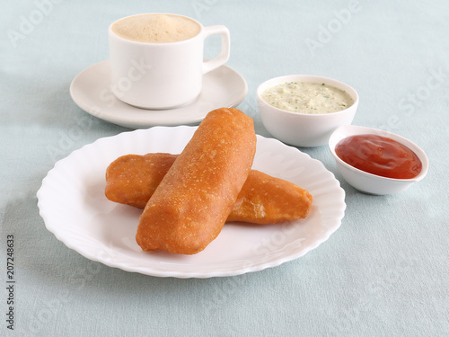 Raw banana bajji or fritter, a popular Indian vegetarian snack, with coconut chutney and tomato ketchup as side dishes and filter coffee.