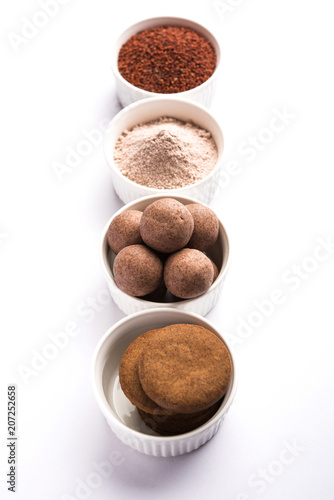 Nachni / Ragi laddu and biscuits or cookies made using  finger millet, sugar and ghee. It's a healthy food from India. Served in a bowl or plate with raw whole and powder. Selective focus
