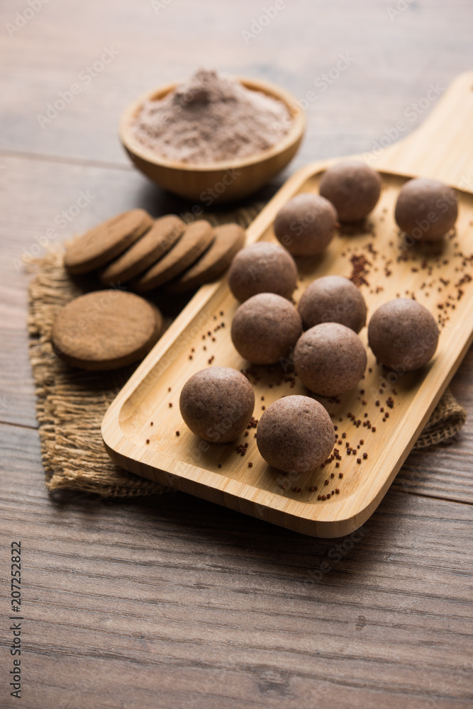 Nachni / Ragi laddu and biscuits or cookies made using finger millet, sugar and ghee. It's a healthy food from India. Served in a bowl or plate with raw whole and powder. Selective focus Nachni / Ragi laddu and biscuits or cookies made using finger millet, sugar and ghee. It's a healthy food from India. Served in a bowl or plate with raw whole and powder. Selective focus