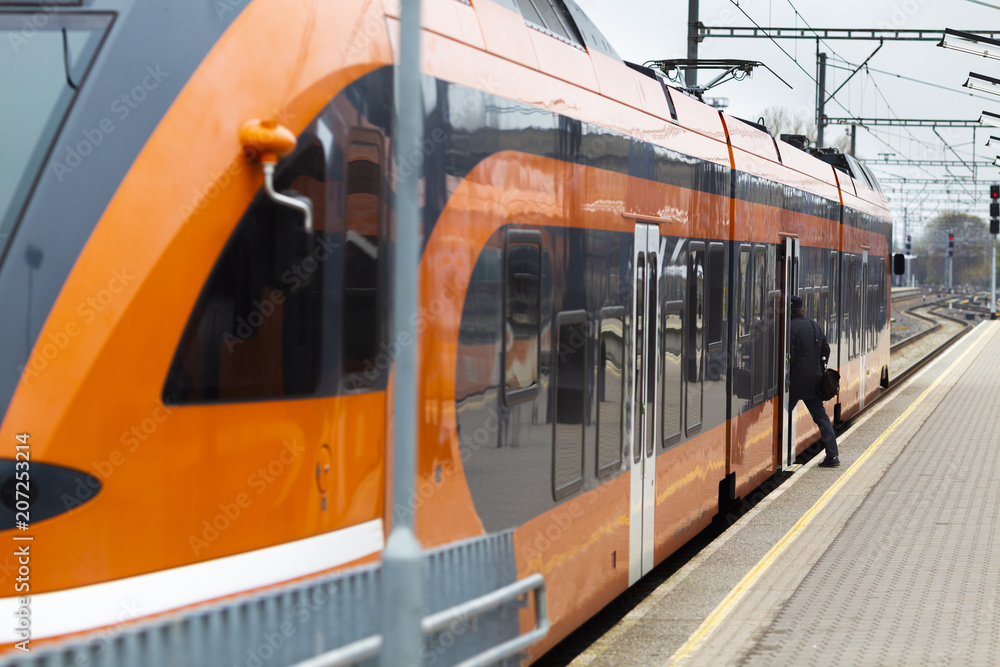 Passenger are entering in modern orange railroad car from station platform.