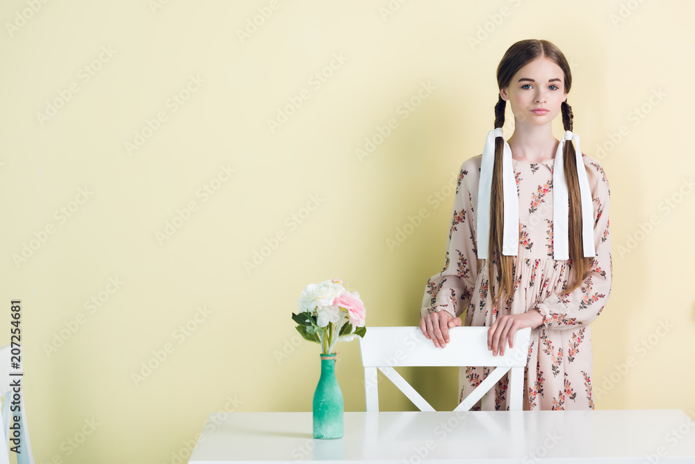 attractive teen girl with braids standing at table with flowers, on yellow attractive teen girl with braids standing at table with flowers, on yellow
