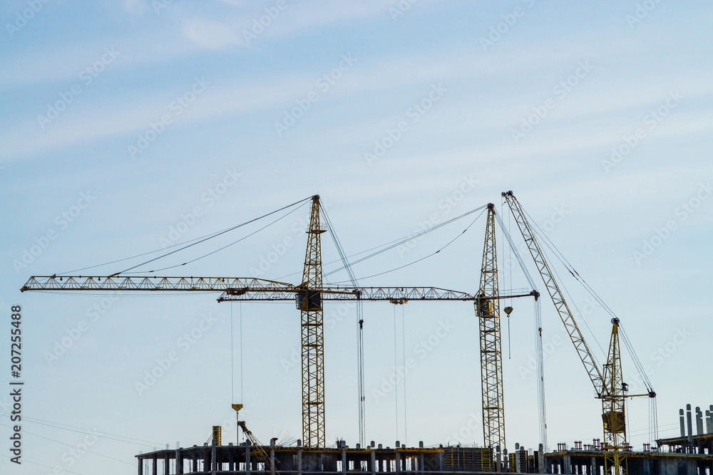 Big tower cranes above buildings under construction against blue sky. Background image of construction close-up with copy space. Build of city.