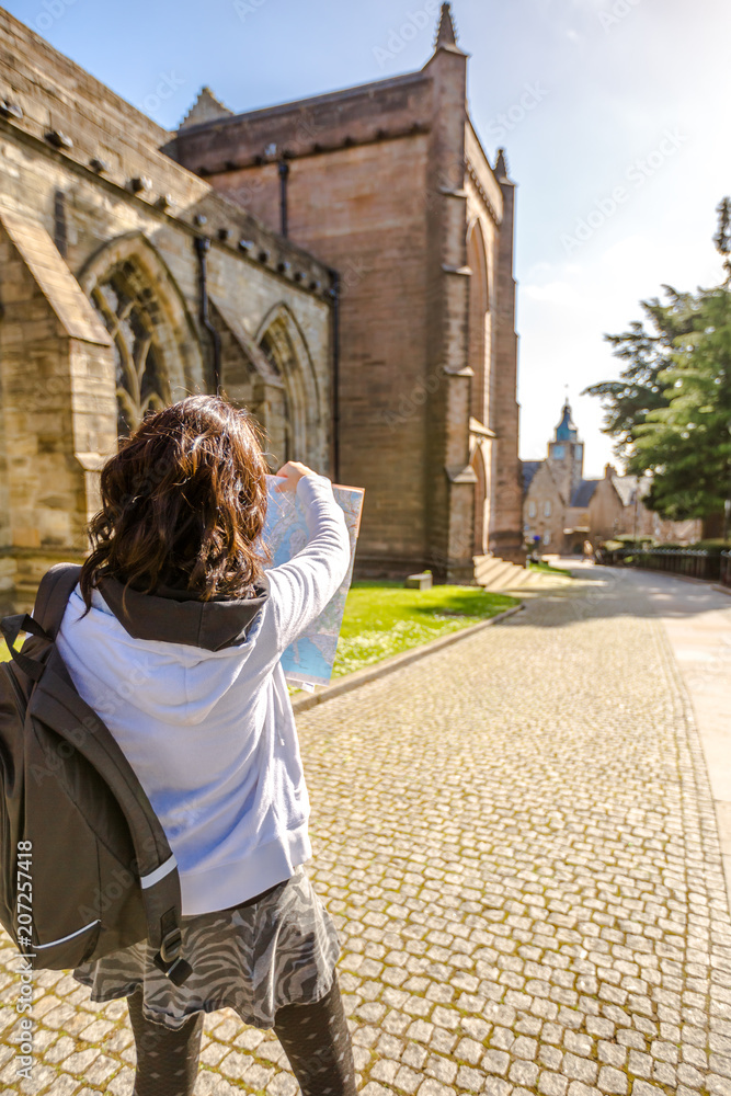 Young woman tourist beside the Church of the Holy Rude in historical Stirling town while browsing a map in a sunny day. Central Scotland, UK, Europe.