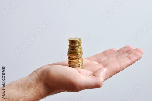 A tall hand of a men holding a stack of money, golden coins, on white background, isolated, side view
