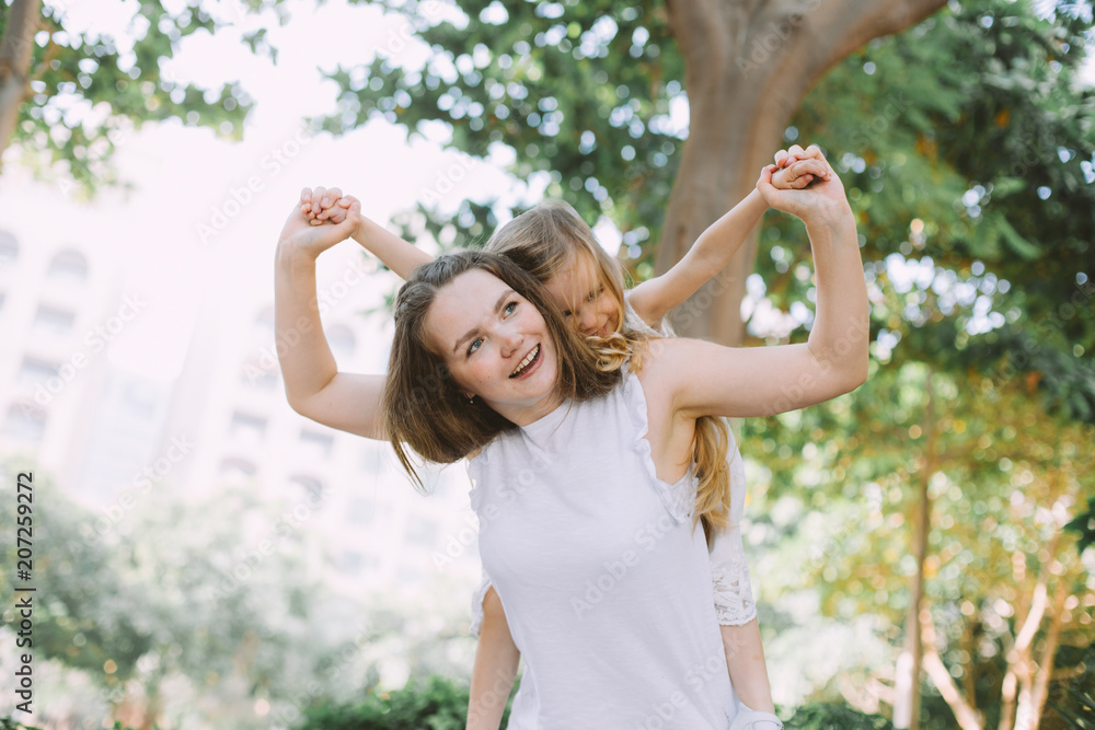 Beautiful young woman her little daughter having fun doing piggyback in summer park Beautiful young woman her little daughter having fun doing piggyback in summer park
