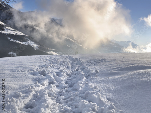 hiking path on the snow in mountain with clouds lightened by the sun 