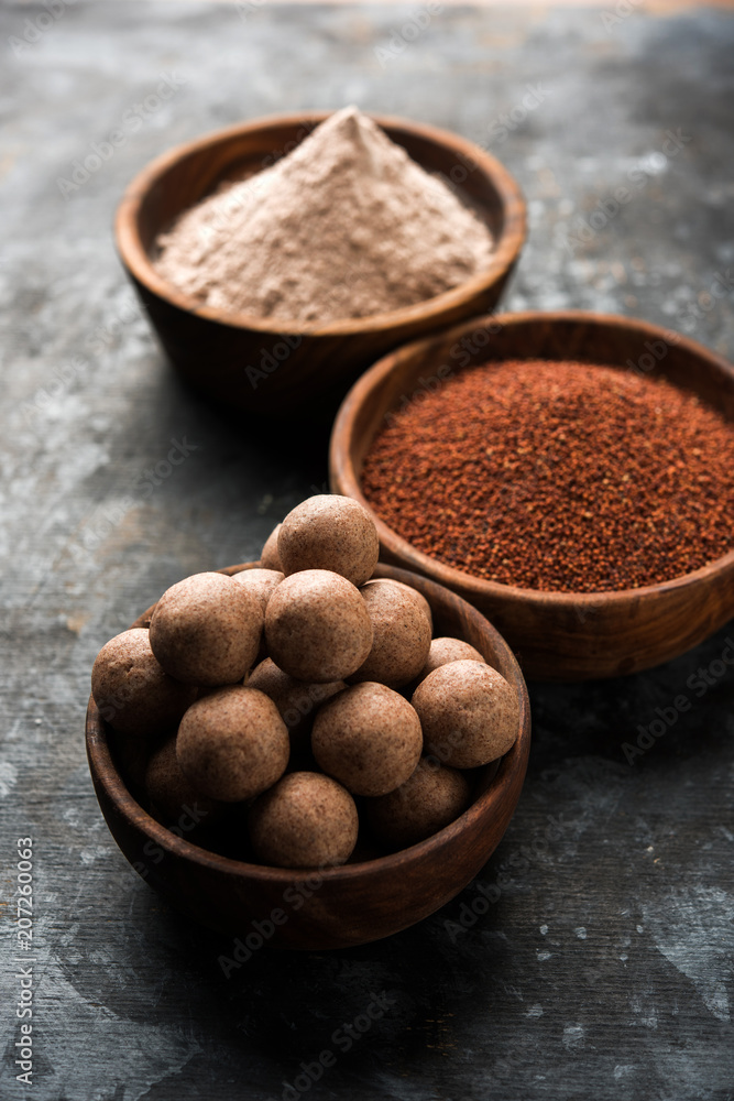 Nachni laddu or Ragi laddoo or balls made using finger millet, sugar and ghee. It's a healthy food from India. Served in a bowl or plate with raw whole and powder. Selective focus Nachni laddu or Ragi laddoo or balls made using finger millet, sugar and ghee. It's a healthy food from India. Served in a bowl or plate with raw whole and powder. Selective focus