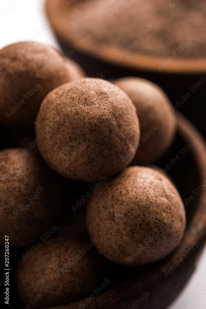 Nachni laddu or Ragi laddoo or balls made using finger millet, sugar and ghee. It's a healthy food from India. Served in a bowl or plate with raw whole and powder. Selective focus Nachni laddu or Ragi laddoo or balls made using finger millet, sugar and ghee. It's a healthy food from India. Served in a bowl or plate with raw whole and powder. Selective focus