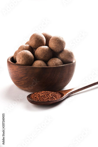 Nachni laddu or Ragi laddoo or balls made using  finger millet, sugar and ghee. It's a healthy food from India. Served in a bowl or plate with raw whole and powder. Selective focus