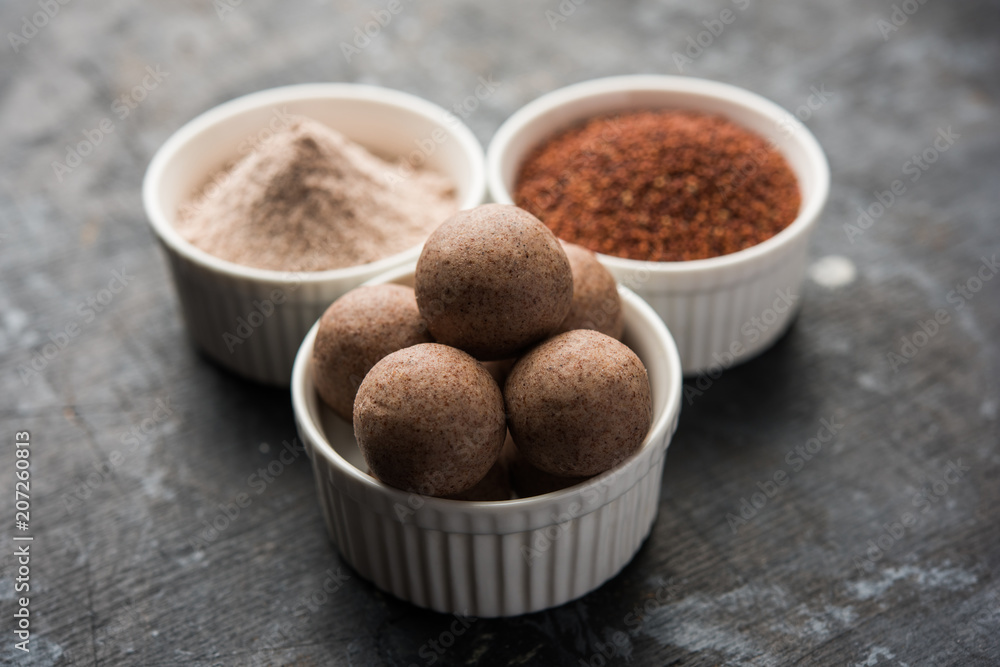 Nachni laddu or Ragi laddoo or balls made using finger millet, sugar and ghee. It's a healthy food from India. Served in a bowl or plate with raw whole and powder. Selective focus Nachni laddu or Ragi laddoo or balls made using finger millet, sugar and ghee. It's a healthy food from India. Served in a bowl or plate with raw whole and powder. Selective focus