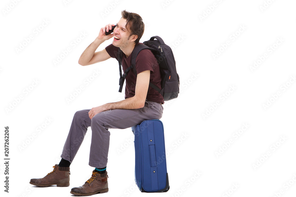 Side portrait of happy traveler talking on cellphone and sitting on suitcase Side portrait of happy traveler talking on cellphone and sitting on suitcase