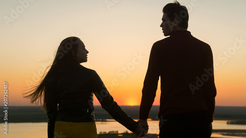 Loving young couple holding hands looking each other at amazing sunset outdoors