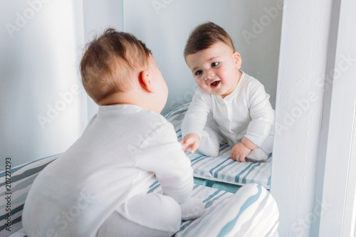 Baby boy sitting near mirror and looking at his reflection photo