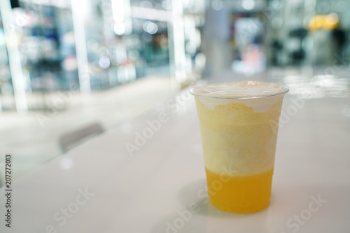 Plastic glass of pineapple smoothie with layer of cream cheese foam on blurred background and copy space, Traditional Taiwanese and Chinese Beverage.