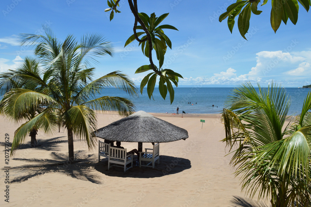 White wooden bungalow surrounded by palm leaves on the beach of amazing lake Malawi or Nyasa in Africa. Perfect peaceful sunny day on the beach of turqouise lake.