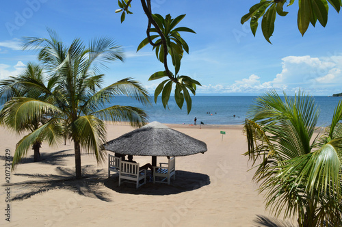 Fototapeta Naklejka Na Ścianę i Meble -  White wooden bungalow surrounded by palm leaves on the beach of amazing lake Malawi or Nyasa in Africa. Perfect peaceful sunny day on the beach of turqouise lake.