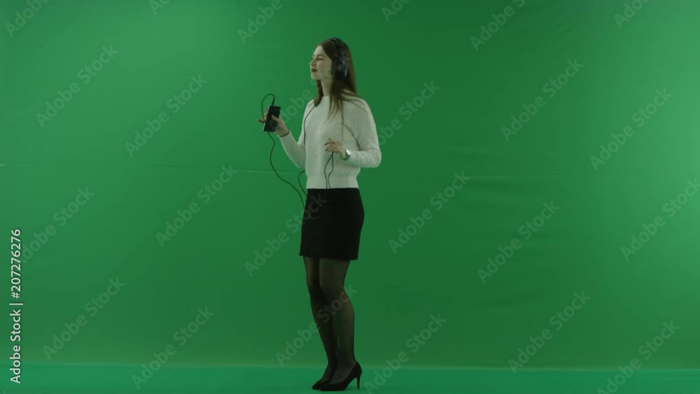 the girl stands in a half-turn, looks at the left, dances with headphones on green screen the girl stands in a half-turn, looks at the left, dances with headphones on green screen