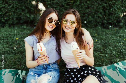 Two pretty brunette girls talking and eating ice cream outdoor on the grass photo