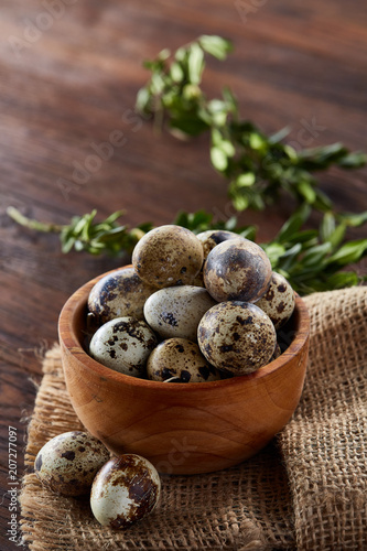 Rural still life with bowl full of eggs quail, eggs on a homespun napkin, boxwood on wooden background, top view photo