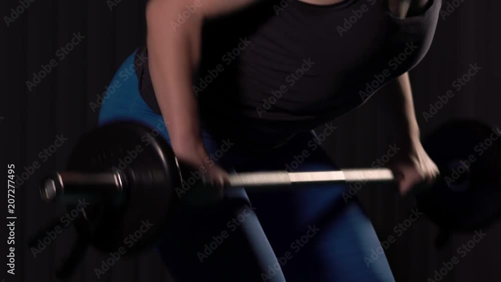 Close-up - Beautiful Young Woman Athlete In Top and Leggings Working Out With Barbell In A Poorly Lit Hall Close-up - Beautiful Young Woman Athlete In Top and Leggings Working Out With Barbell In A Poorly Lit Hall