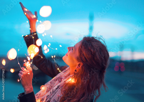 Happy woman playing with fairy light garland at evening
