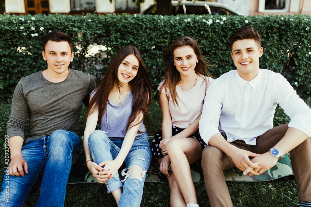 Obraz premium Two couples sitting on the loan in the park smiling and having fun on summer days