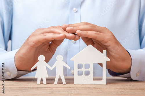 Insurance of a young family and house. Man in shirt covers his hands with couple of two men and woman and house