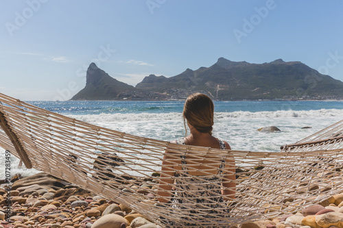 Beautiful woman on hammock on rocky shoreline with view of Hout Bay in Cape Town