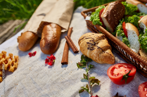 Picnic basket full with sandwiches, baguette and croissant on a homespun tablecloth, flat lay, selective focus