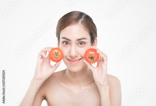 beautiful asia woman with towel on head with perfect clean skin smiling holding tomato slices over white background. Beauty cosmetology and spa.