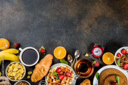 Healthy breakfast eating concept, various morning food - pancakes, waffles, croissant oatmeal sandwich and granola with yogurt, fruit, berries, coffee, tea, orange juice, dark rusty background