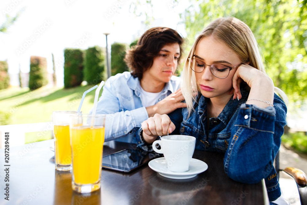 Frustrated angry blond woman turned her back ignoring boyfriend while they sitting together at cafe's garden Frustrated angry blond woman turned her back ignoring boyfriend while they sitting together at cafe's garden