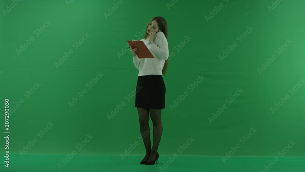 the girl stands in a half-turn, looks at the left, talks on the phone and makes notes on green screen the girl stands in a half-turn, looks at the left, talks on the phone and makes notes on green screen