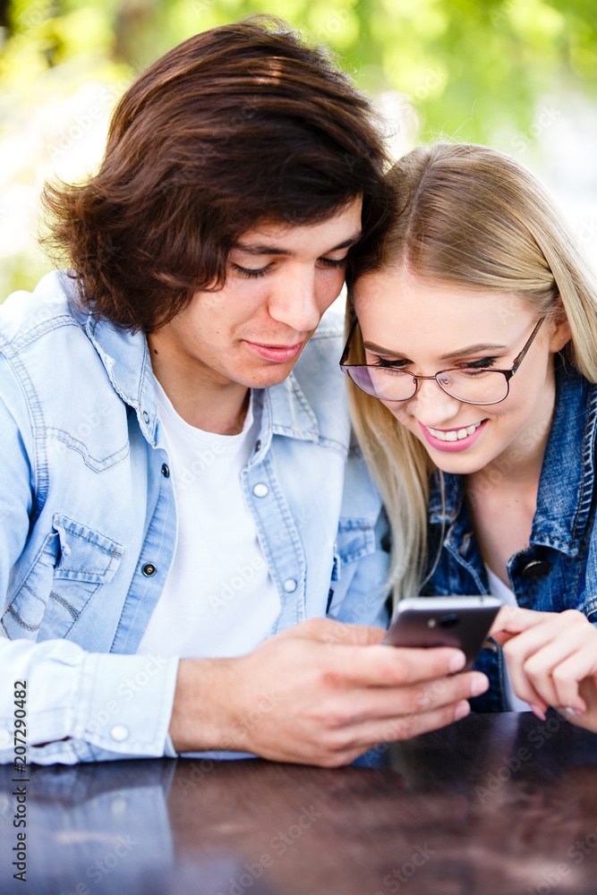 Couple spending valentines day on social networks, using phone device while sitting together at cafe Couple spending valentines day on social networks, using phone device while sitting together at cafe