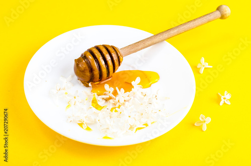 Plate with honey and spoon on yellow background