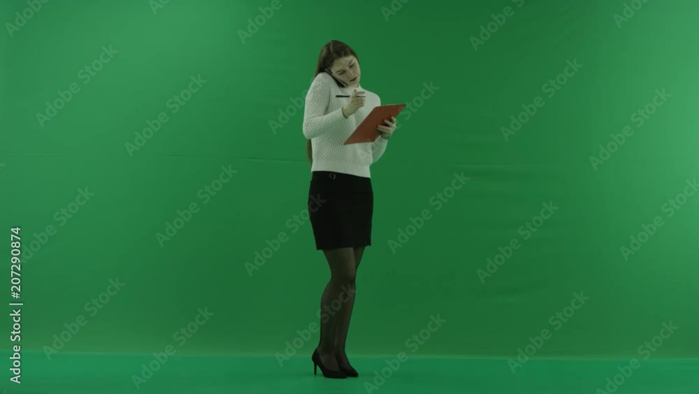 the girl stands in a half-turn, looks at the right, talks on the phone and makes notes on green screen the girl stands in a half-turn, looks at the right, talks on the phone and makes notes on green screen