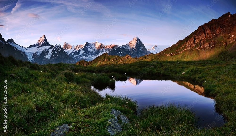 Mountain lake, reflection of high mountains, lawn in the middle of the mountains