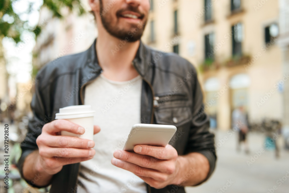 Cropped blurry image of caucasian adult man 30s wearing casual clothing drinking takeaway coffee, and using cell phone in downtown Cropped blurry image of caucasian adult man 30s wearing casual clothing drinking takeaway coffee, and using cell phone in downtown