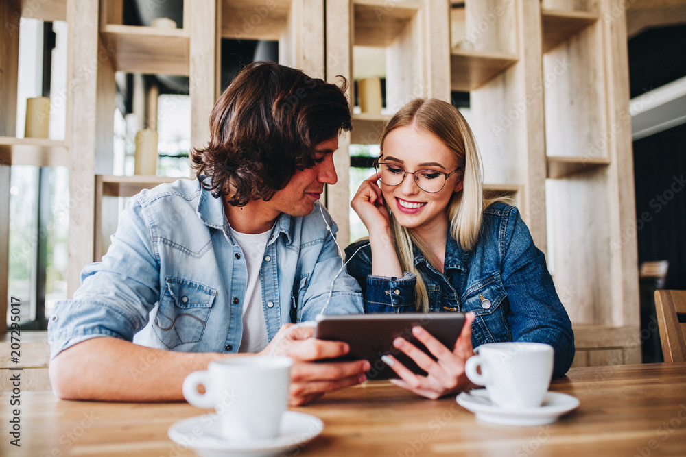 Young Charming Couple Using Tablet While Sitting Together And Drinking Coffee Young Charming Couple Using Tablet While Sitting Together And Drinking Coffee
