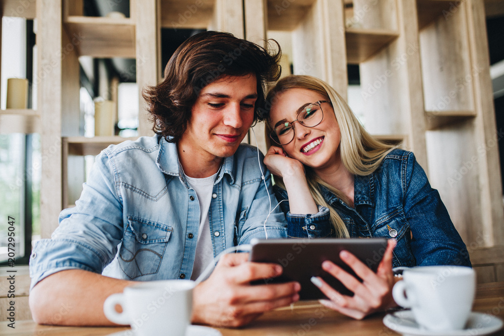 Young Charming Couple Using Tablet While Sitting Together And Drinking Coffee Young Charming Couple Using Tablet While Sitting Together And Drinking Coffee