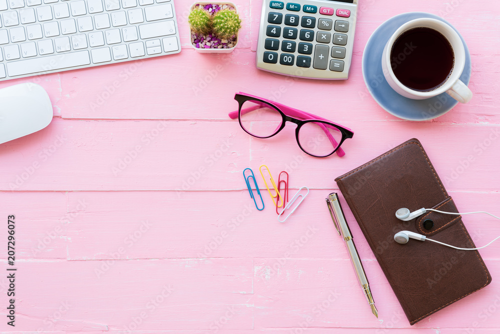Top view office table with workspace and office accessories including calculator, keyboard, glasses, clips, flower, pen, note book, Earphone and coffee on pink wooden background. Top view office table with workspace and office accessories including calculator, keyboard, glasses, clips, flower, pen, note book, Earphone and coffee on pink wooden background.