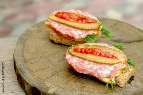 Two sandwiches with sausage, cheese and dill on a wooden stump. Selective focus.