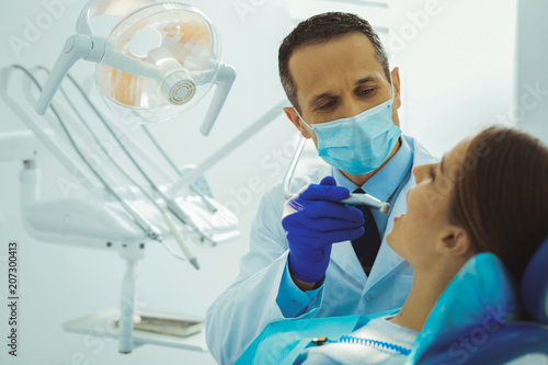 Treating you. Attentive man being in medical uniform while working with his patient