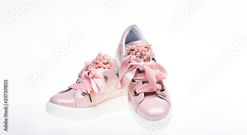 Footwear for girls and women decorated with pearl beads. Pair of pale pink female sneakers with velvet ribbons. Cute shoes isolated on white background. Trendy sneakers concept.